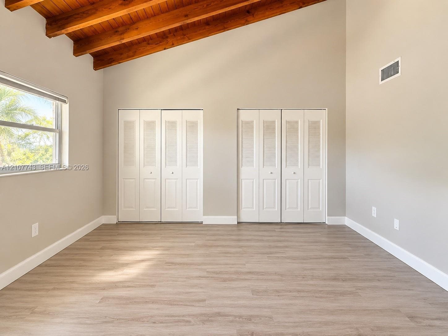 Vaulted ceiling with exposed wood beams, wood-finish flooring, and dual sets of bi-fold louvered closets