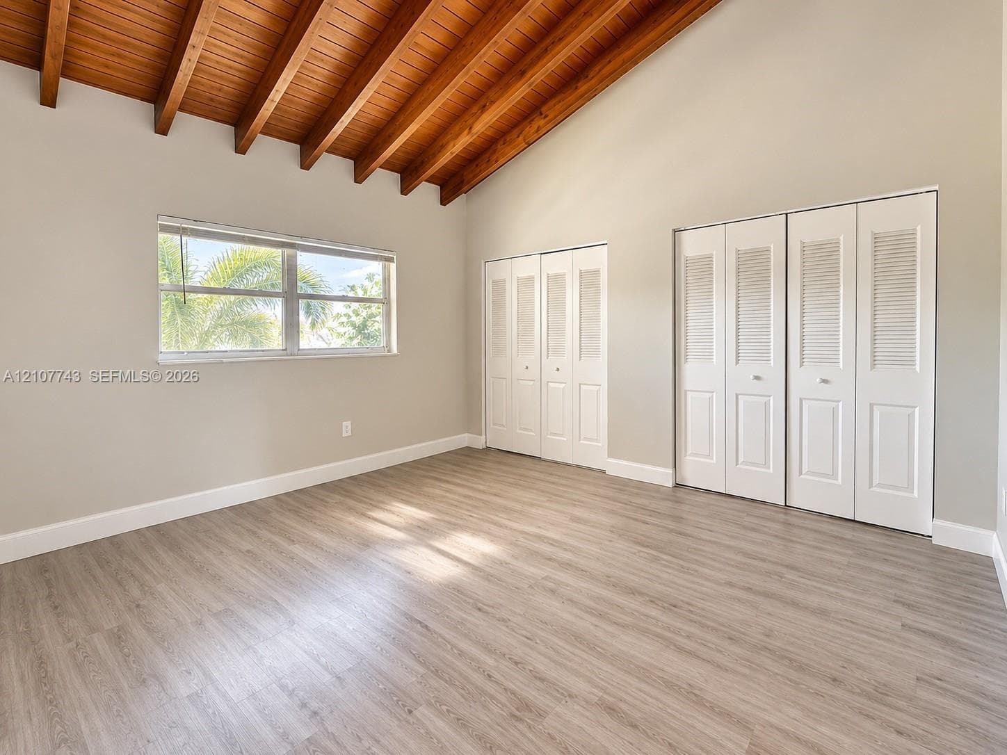Vaulted ceiling with exposed wood beams, wood-finish flooring, and dual bi-fold louvered closets