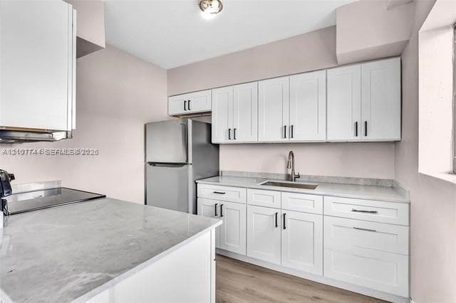 Kitchen featuring white shaker-style cabinetry, solid-surface countertops, a stainless steel refrigerator, an integrated sink with a pull-down faucet, and wood-finish flooring