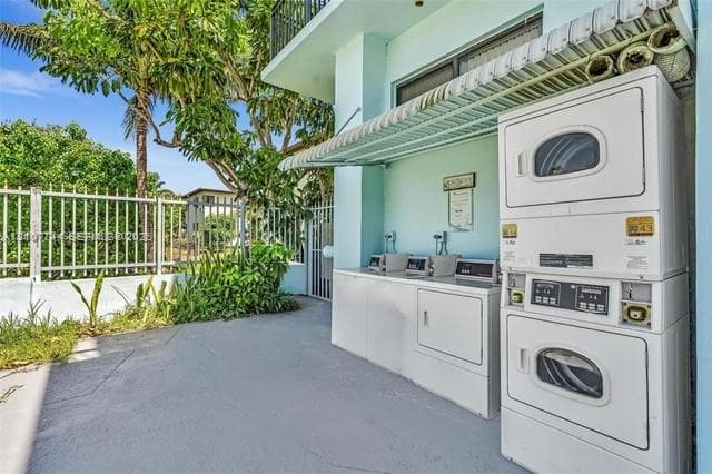 Outdoor laundry area featuring stacked and side-by-side white washer and dryer units, concrete flooring, and metal protective awning under a covered exterior structure