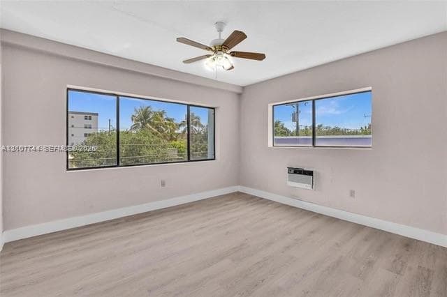 Interior space featuring neutral wall paint, wood-finish flooring, a ceiling fan with integrated lighting, and multiple windows