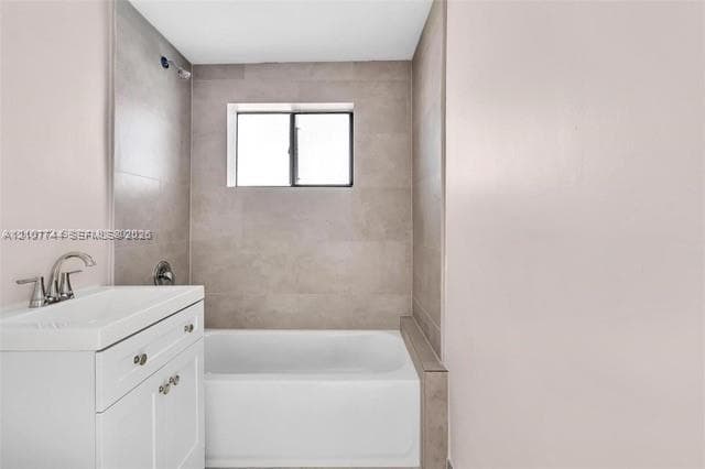 Bathroom featuring a white vanity cabinet with a rectangular basin, chrome faucet, bathtub with surround tiling, and a window