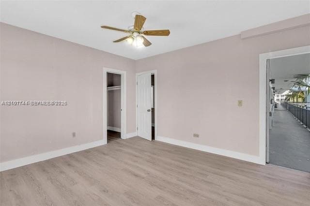 Interior room featuring wood-finish flooring, a ceiling fan with integrated lighting, a built-in closet, and a doorway opening to an exterior walkway