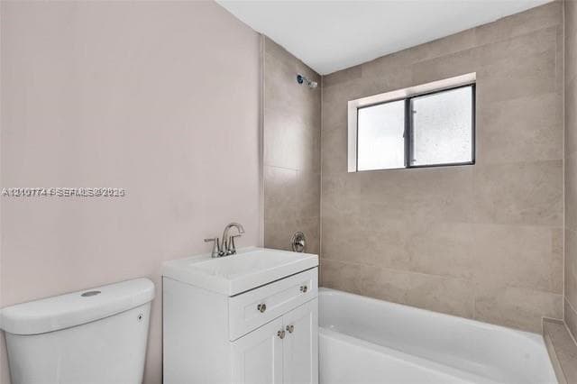 White vanity with a rectangular sink, dual-handle faucet, integrated tub-shower combination, and floor-to-ceiling neutral tile surround