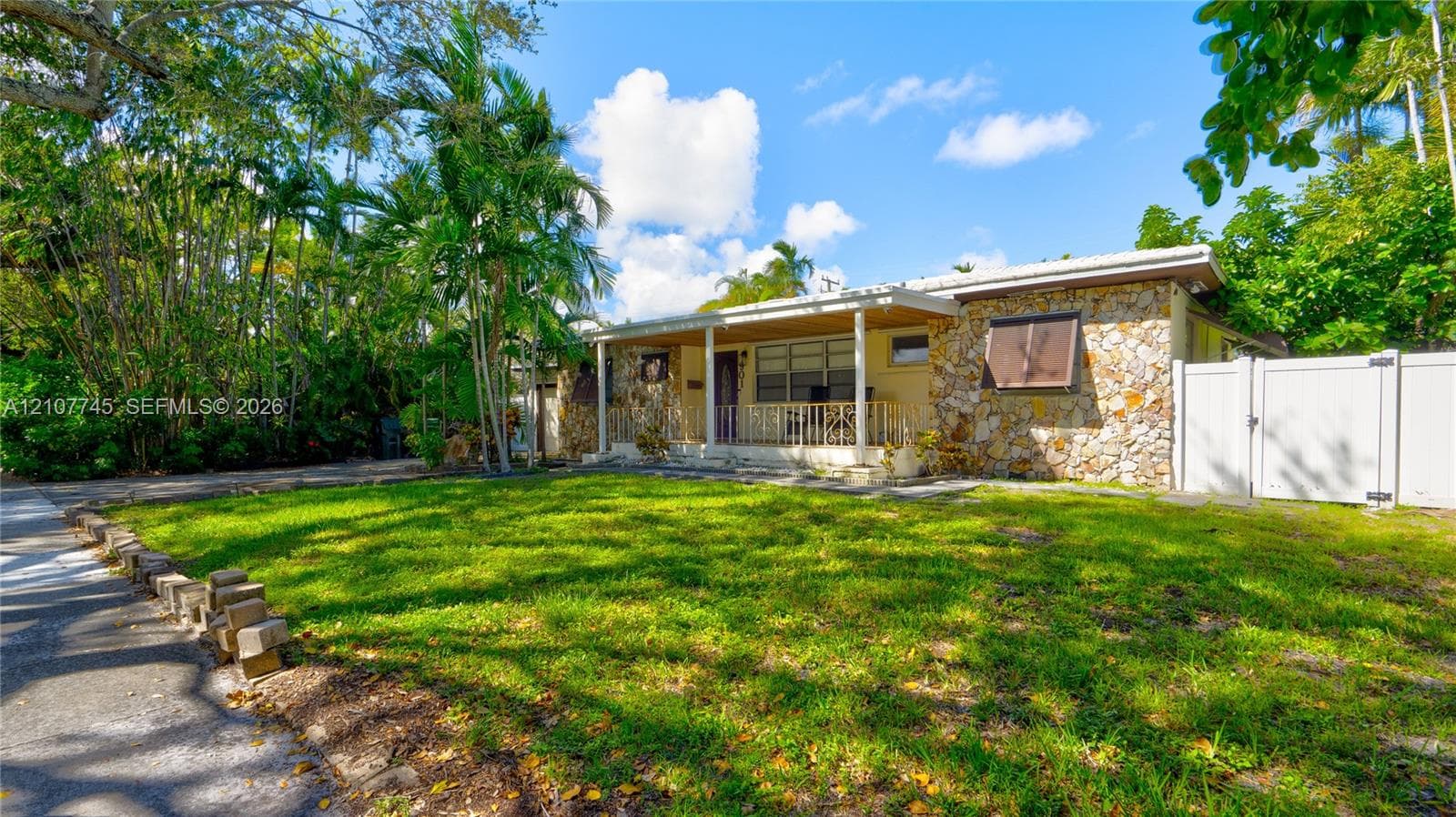 Single-story exterior featuring natural stone veneer, a covered front porch, and a white privacy fence