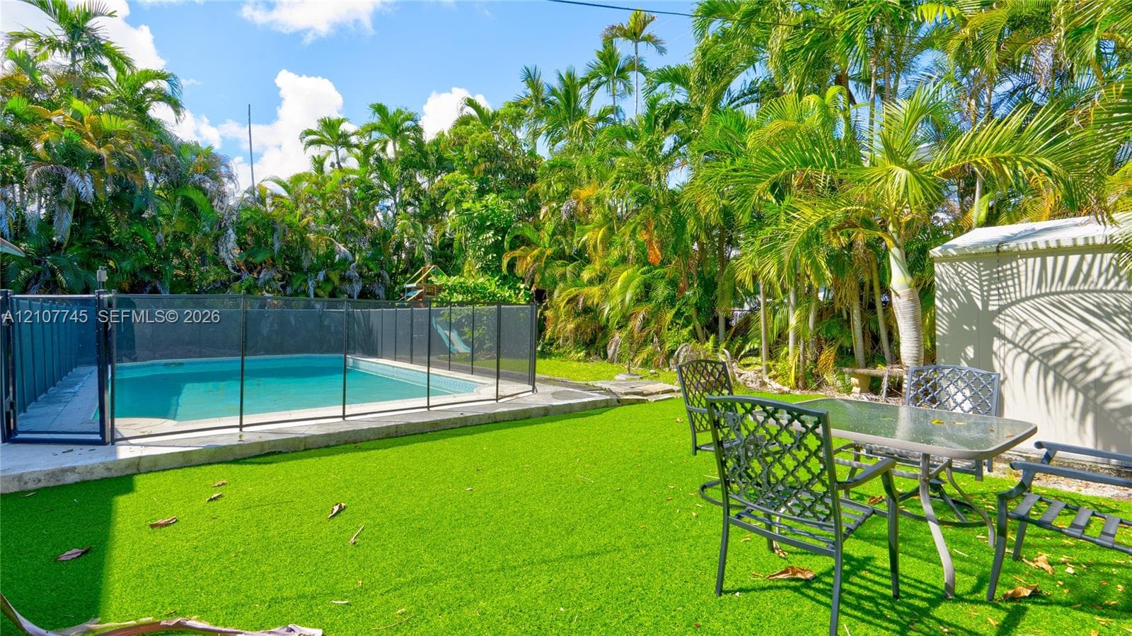 Outdoor space featuring a swimming pool with a protective mesh enclosure, synthetic turf lawn, and mature palm trees
