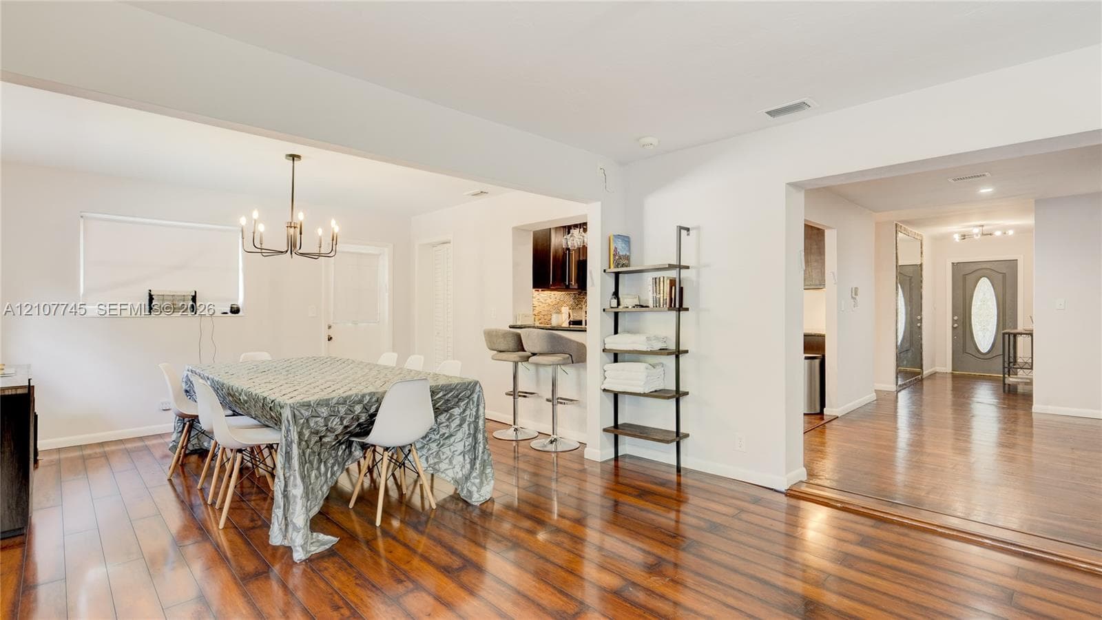 Wood-finish flooring, multi-light chandelier, pass-through breakfast bar, dark-finish cabinetry, and entry door with glass inset