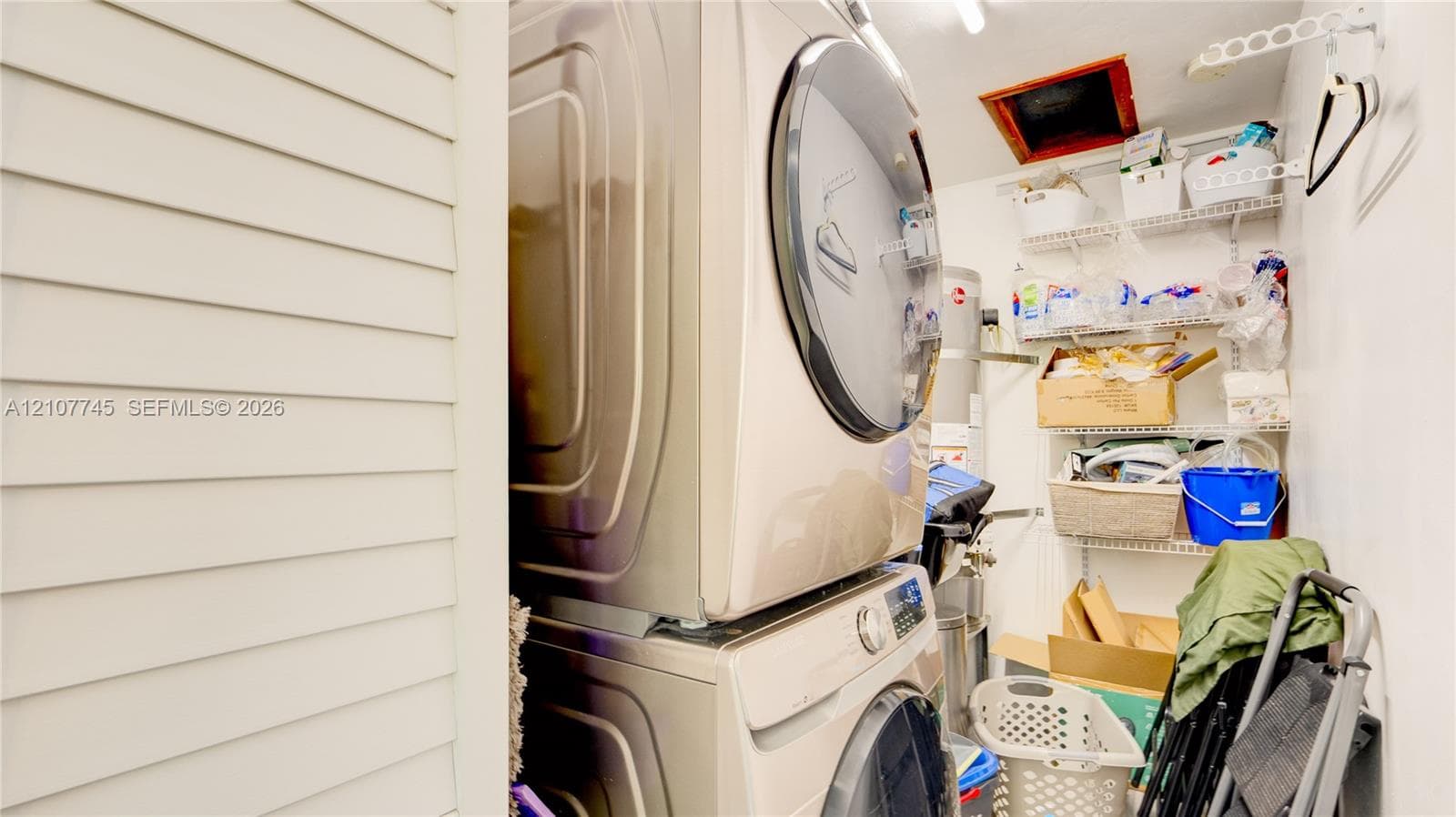Stacked high-efficiency laundry appliances, louvered closet door, and tiered wire shelving