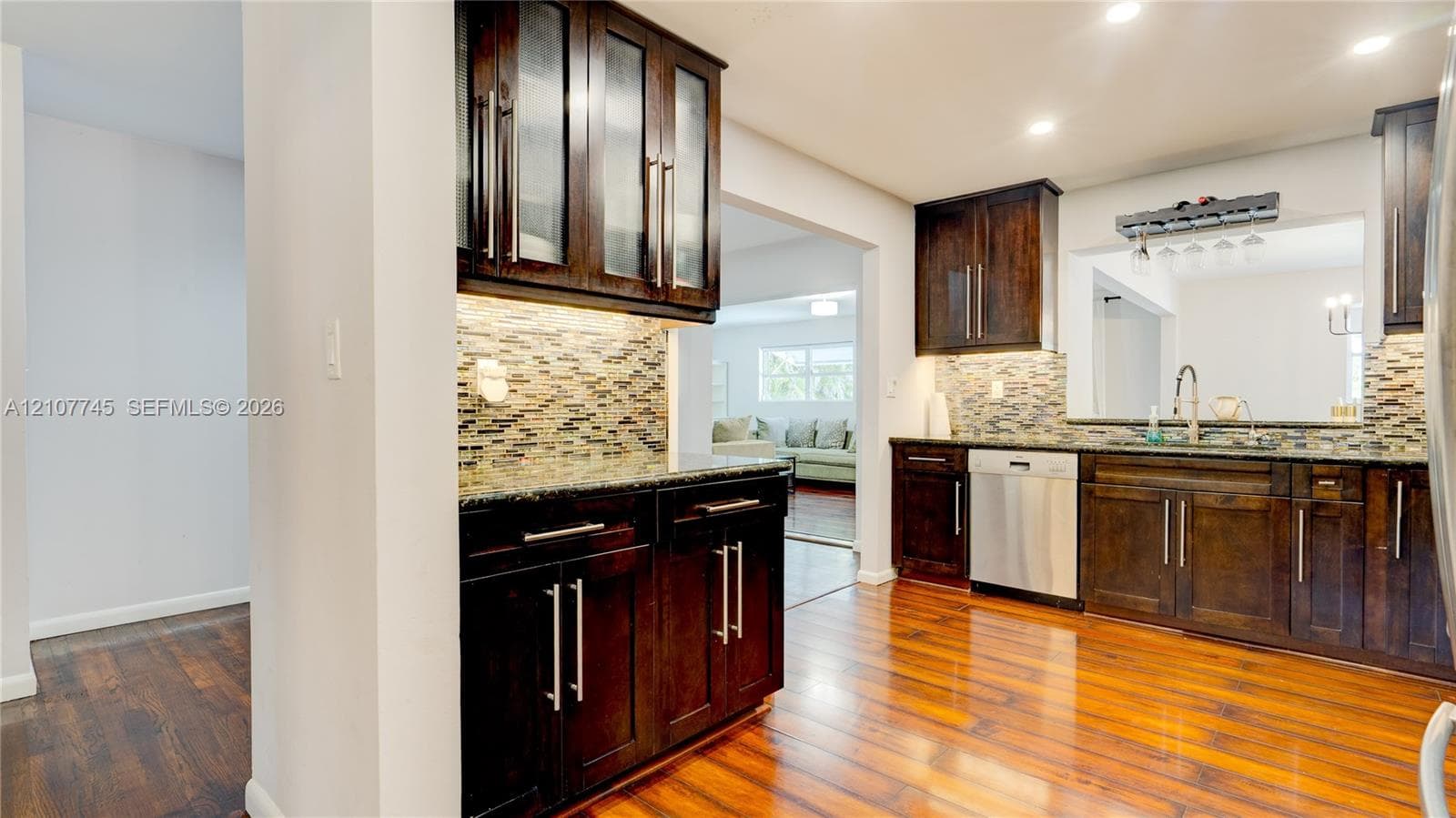 Kitchen featuring dark-finish cabinetry with glass-panel upper doors, stone countertops, integrated tiled backsplash, stainless steel appliances, and wood-finish flooring