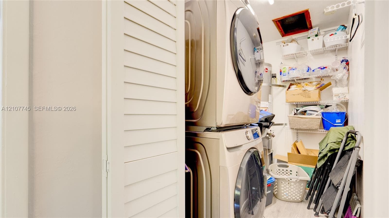 Laundry closet featuring stacked front-load appliances and tiered wire shelving