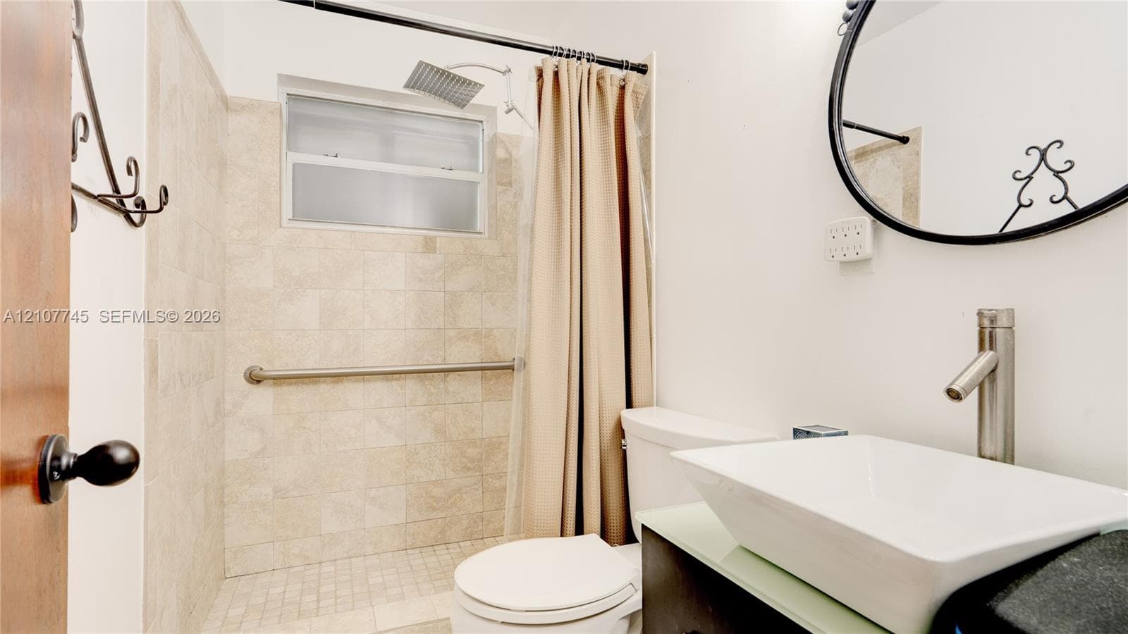 Bathroom featuring a vessel sink with a tall-profile faucet, vanity with a light-toned countertop, shower with stone-tile surround, and ceiling-mounted rainfall showerhead