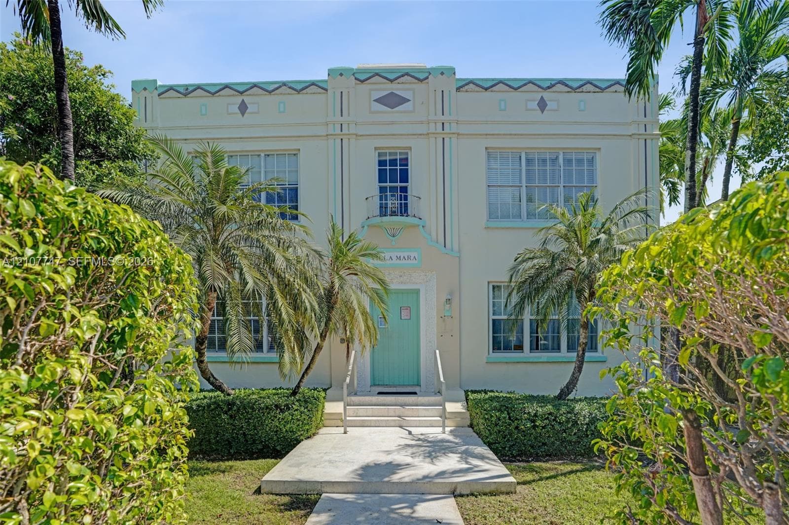Art Deco exterior featuring geometric facade detailing, a central second-story balcony, symmetrical multi-pane windows, and a concrete entrance walkway