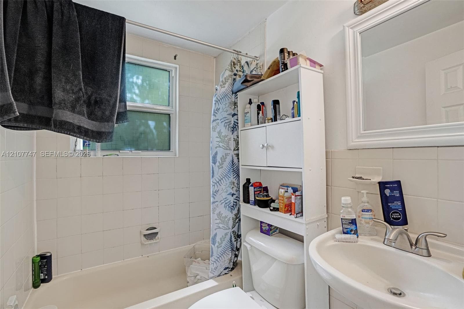 Bathroom featuring a wall-mounted rectangular mirror, pedestal sink with double-handle faucet, tiled shower enclosure, and integrated window