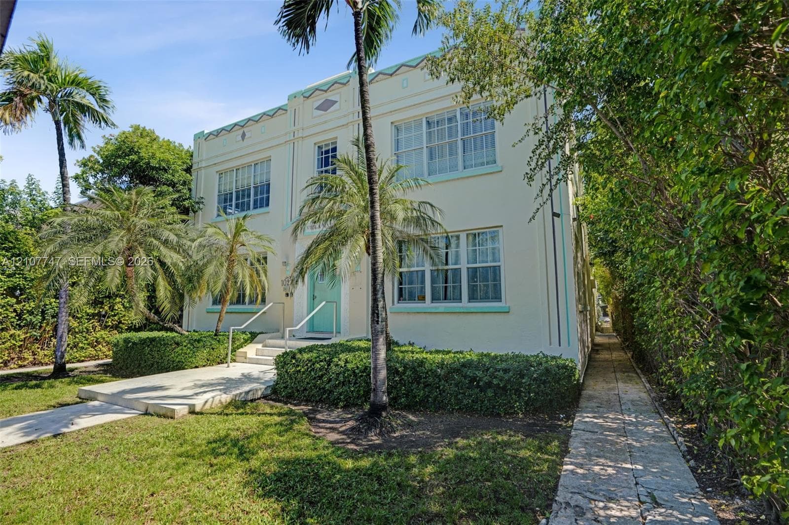 Art Deco exterior featuring cream-colored stucco facade, geometric cornice detailing, multi-pane windows, and a central entryway with a concrete staircase