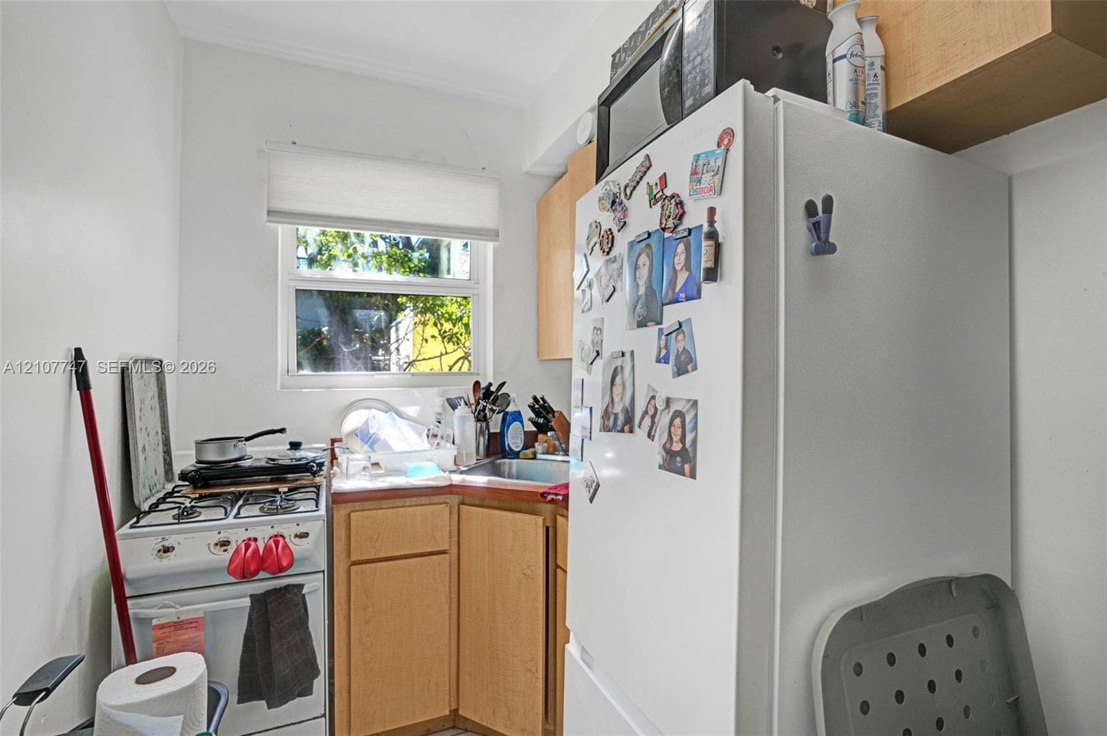 Kitchen featuring light-finish wood cabinetry, a stainless steel sink, a gas range, and a window with a roller shade