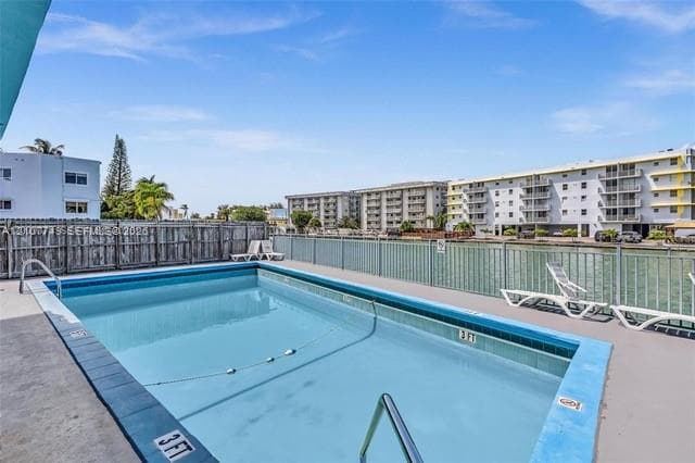 In-ground swimming pool featuring a concrete deck, metal perimeter fencing, and water frontage