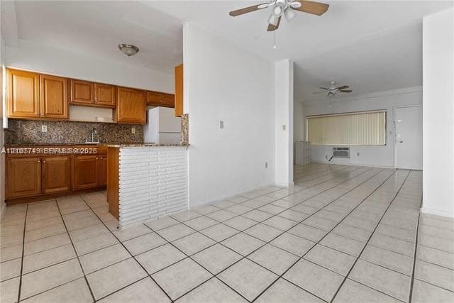 Kitchen featuring wood cabinetry, stone-finish countertops, and a white brick-accented peninsula, complemented by neutral tile flooring throughout the interior