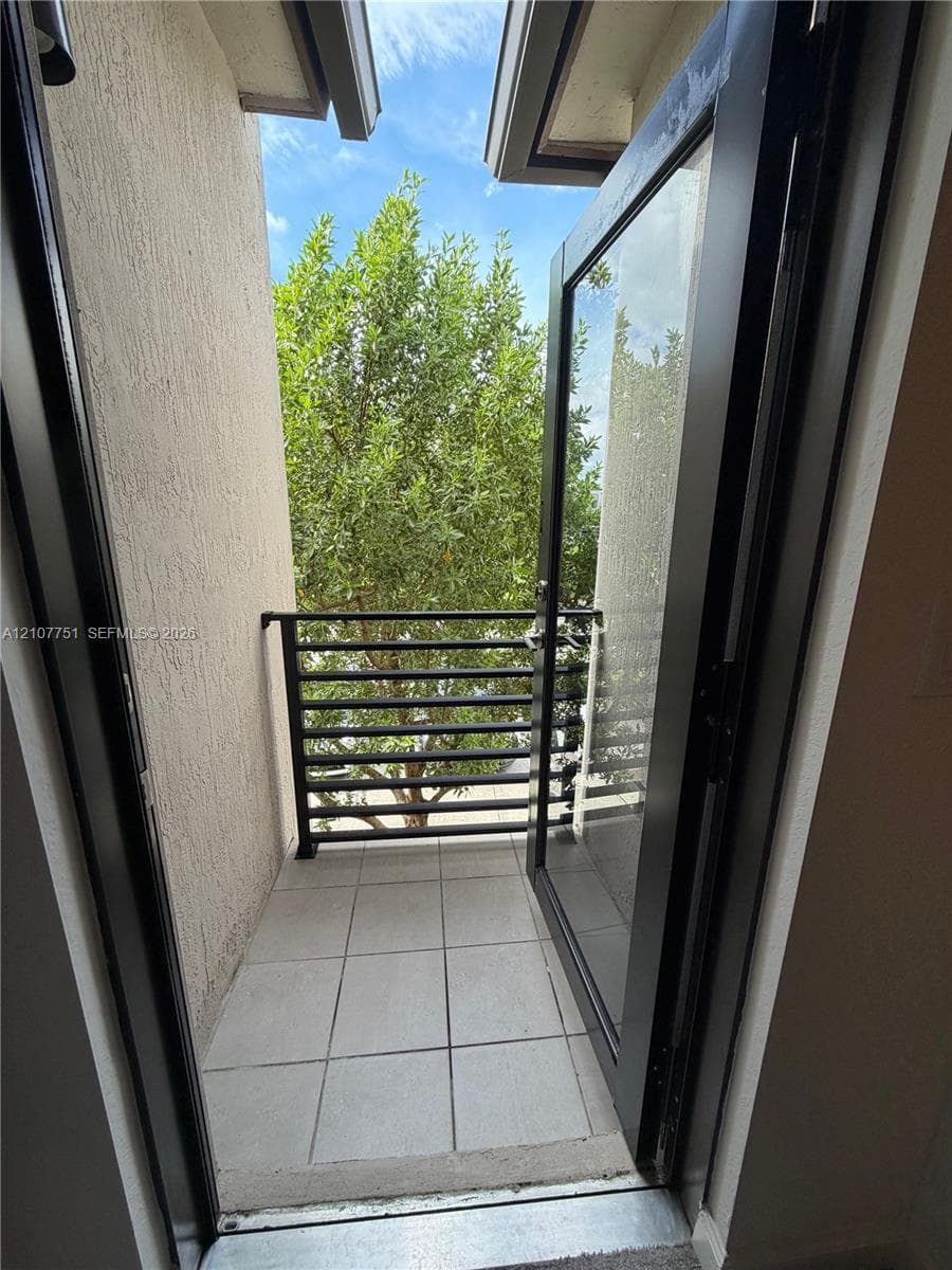 Balcony featuring a matte black metal railing, tiled flooring, textured stucco walls, and a glass-paneled door