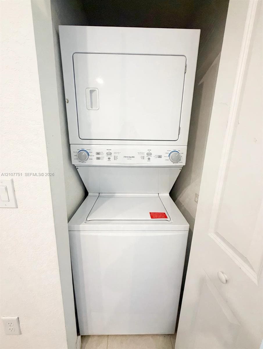 Stacked white washer and dryer unit located within a recessed closet enclosure