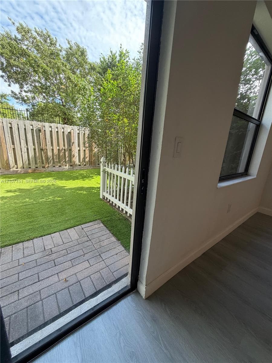 Backyard featuring a paved stone patio, synthetic turf lawn, white picket fencing, and a perimeter privacy fence
