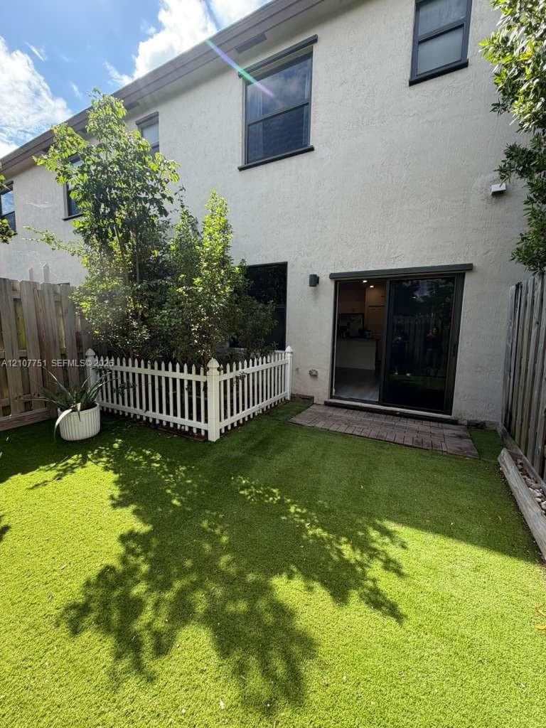 Enclosed backyard featuring synthetic turf, wood-tone privacy fencing, a white picket-style enclosure, and a paved patio area