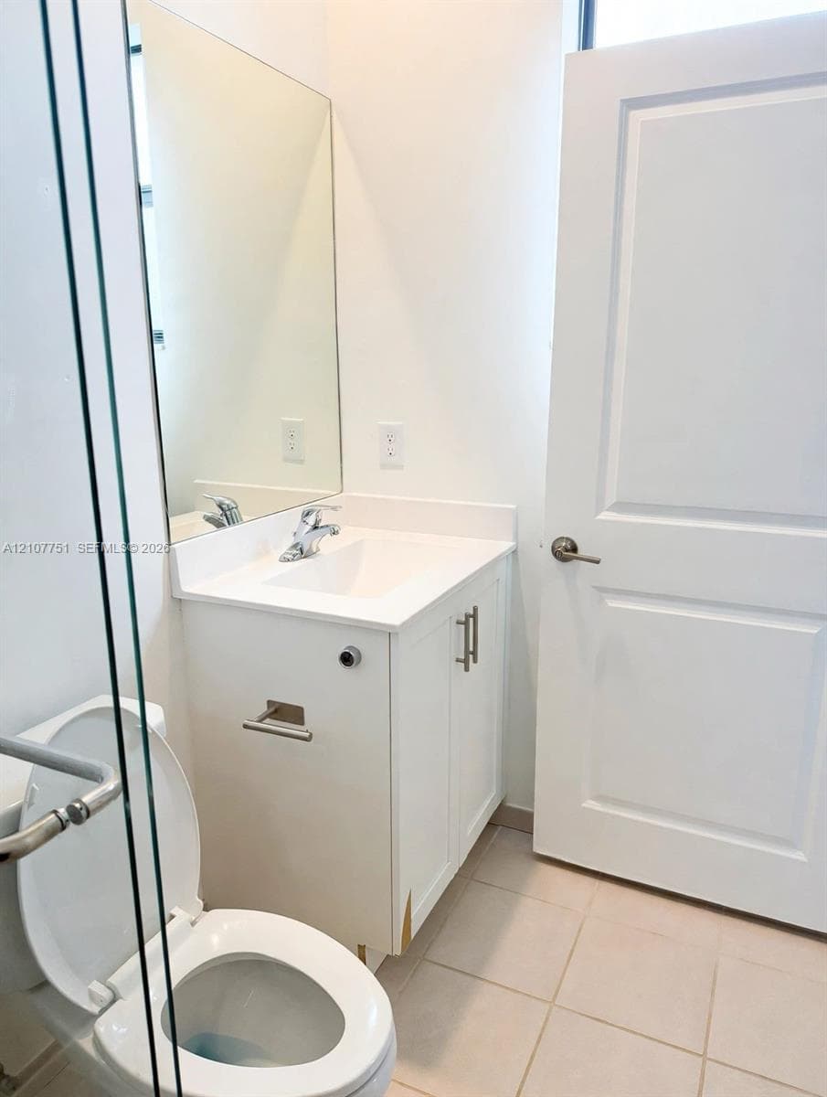 Bathroom featuring a vanity with white cabinetry, a solid-surface countertop with an integrated sink, a full-length wall mirror, tile flooring, and a glass-enclosed shower