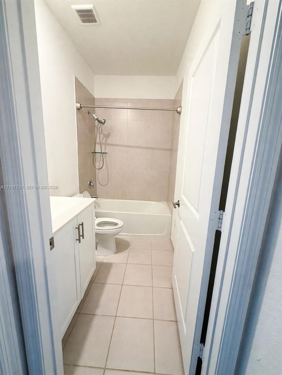 Bathroom featuring a white vanity cabinet with a solid surface countertop, ceramic tile flooring, a shower-tub combination with tiled surround, and a chrome hand-held shower fixture