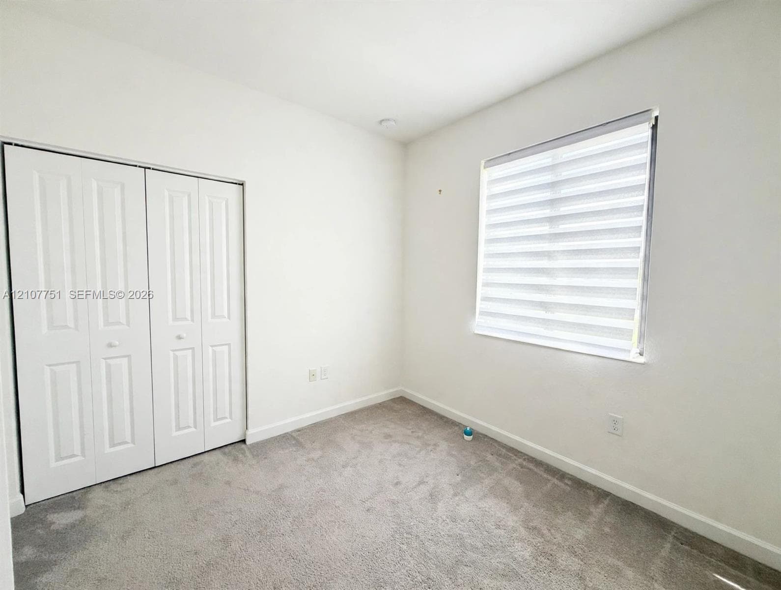 Neutral-toned carpeting, white walls, dual-paneled closet doors, and a window fitted with horizontal layered shades