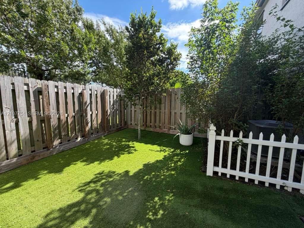 Enclosed backyard featuring synthetic turf, vertical wood fencing, and white picket fencing