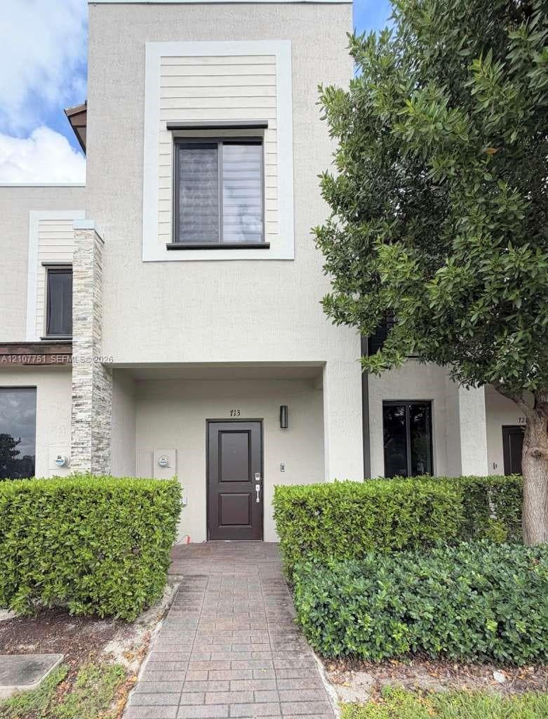 Stucco facade featuring horizontal siding accents, stone veneer pillars, a paved entryway, and a solid-panel front door