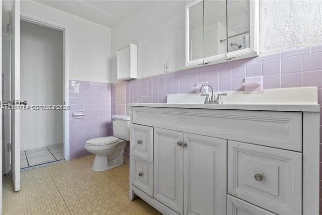 White painted wood vanity with integrated countertop, ceramic tile wall surround, medicine cabinet with mirrored doors, and built-in wall-mounted soap dish