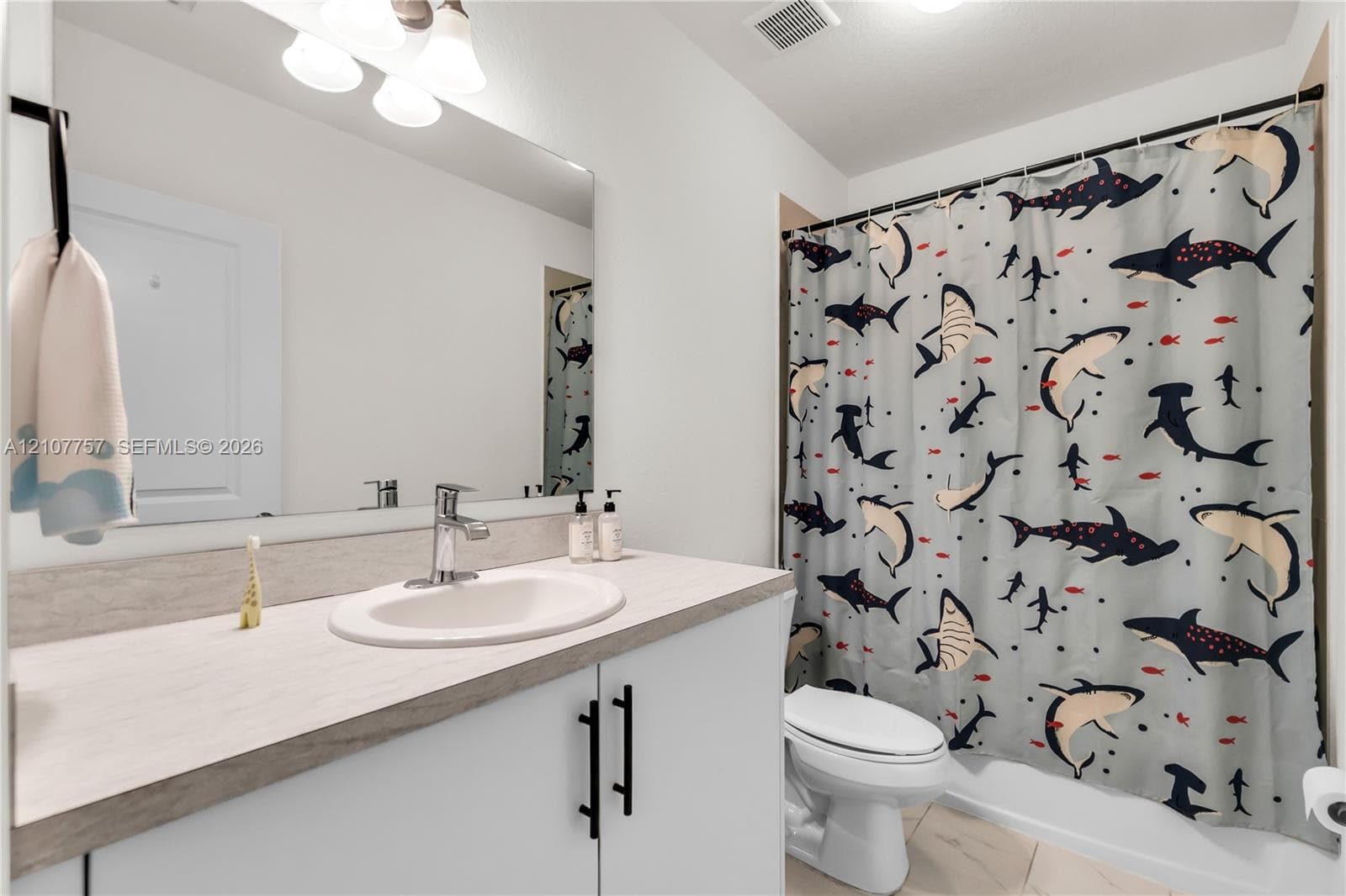 Bathroom featuring a vanity with a light-toned countertop, integrated basin, matte black hardware, a wall-to-wall mirror, and overhead track lighting