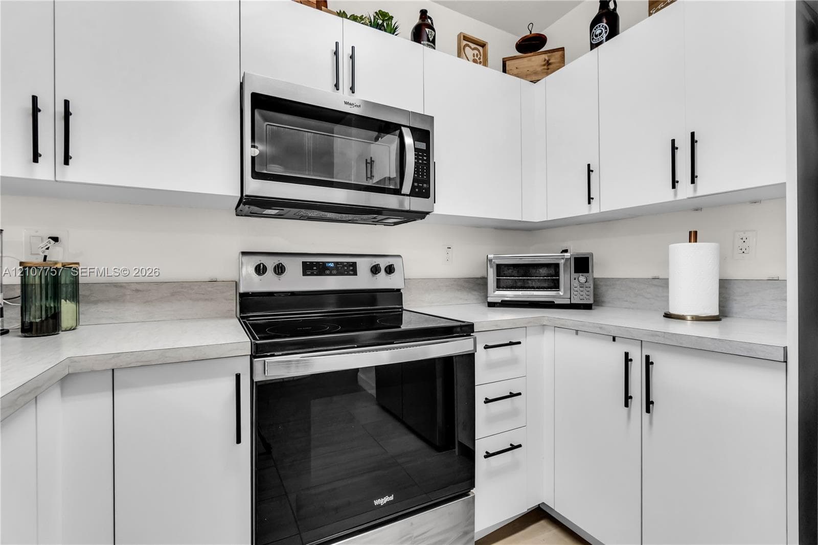 White shaker-style cabinetry with matte black hardware, light-toned countertop, and integrated stainless steel microwave and electric range