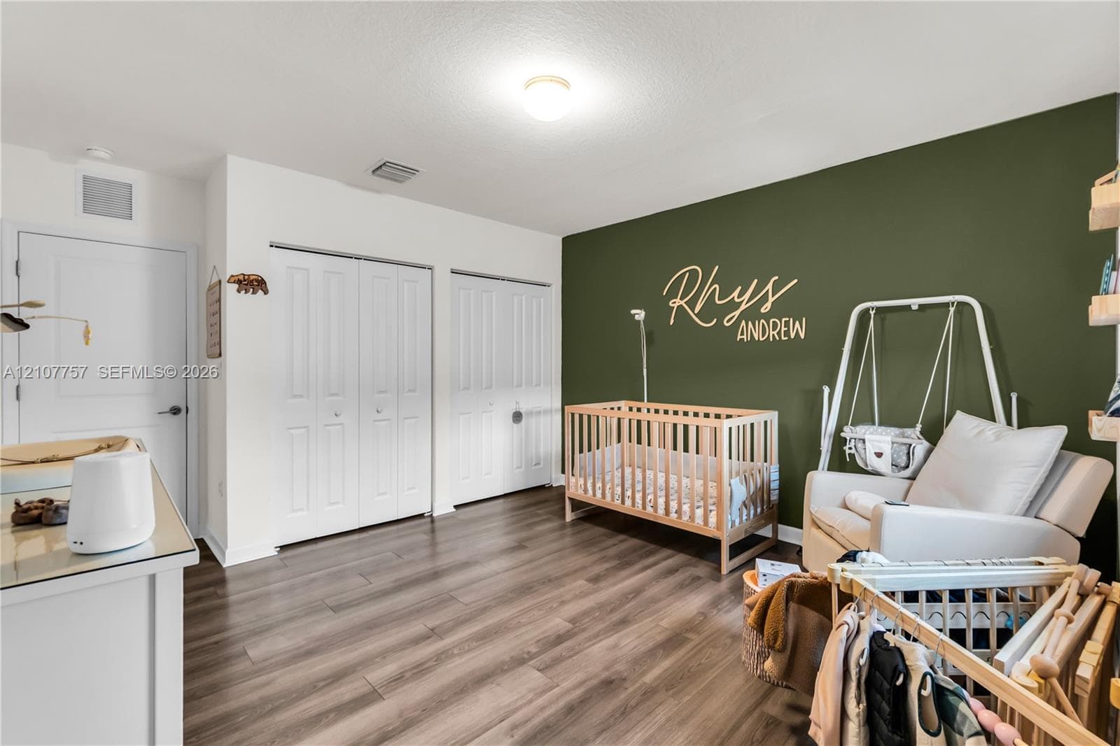 Room featuring wood-finish flooring, two sets of double-door closets, and an accent wall finished in a deep olive tone