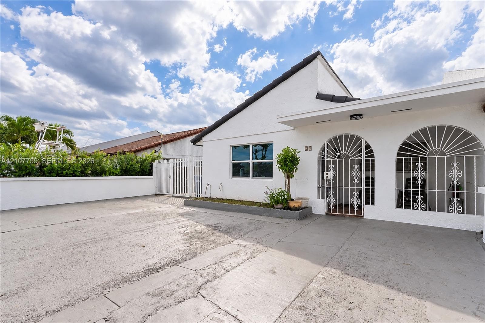 Exterior facade featuring a white stucco finish, arched metal security grilles, a concrete driveway, and a raised concrete garden planter