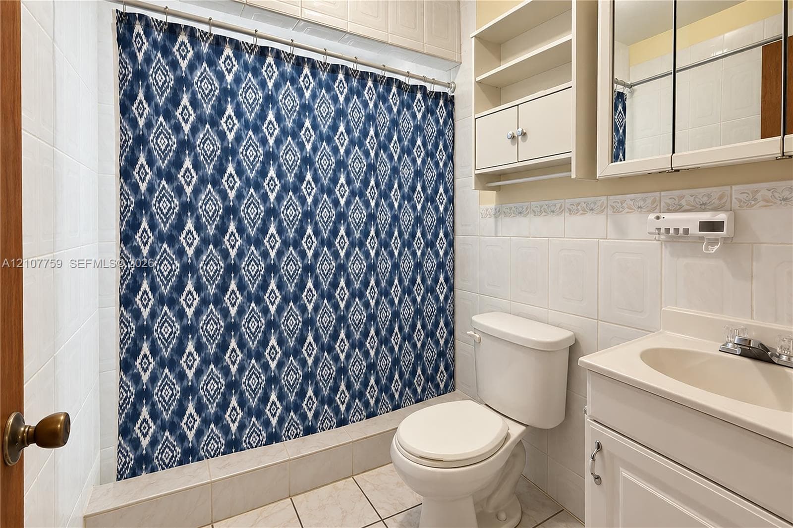 Full-height ceramic wall tiling, white vanity with integrated sink, dual-door medicine cabinet with integrated shelving, and tiled flooring