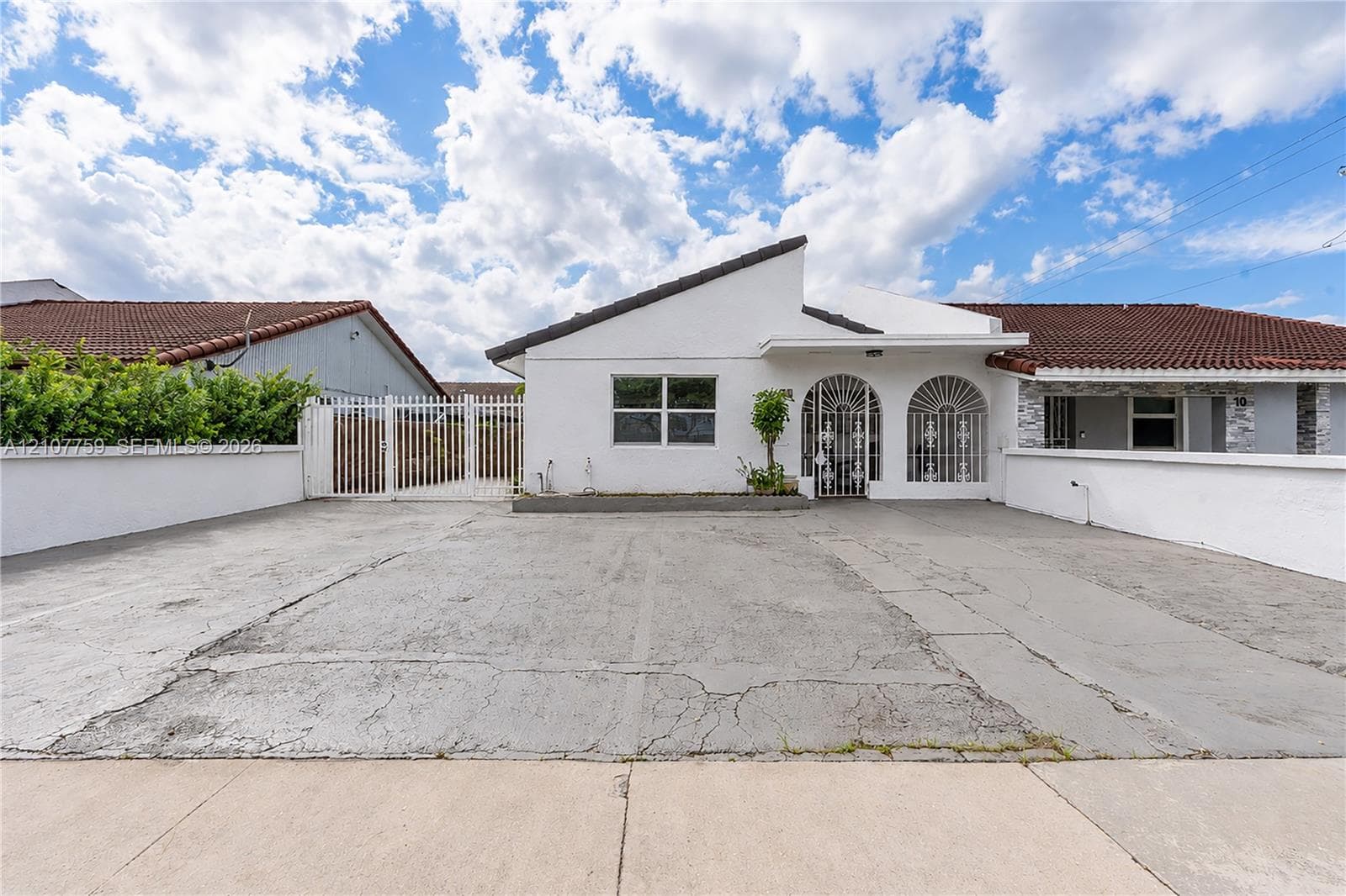 Dual arched entryways with decorative security grilles, a pitched roof with terracotta-style tiles, and a gated side perimeter