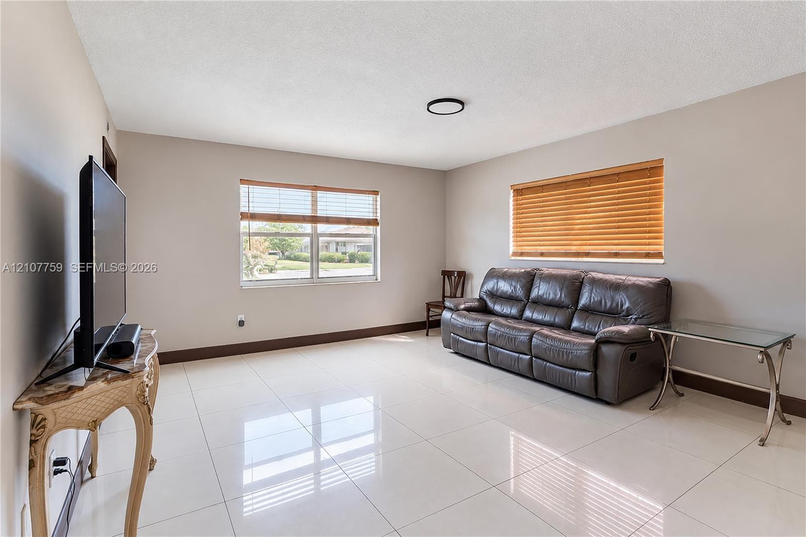 Living area featuring large-format tile flooring, neutral wall paint, and dual windows with built-in blinds