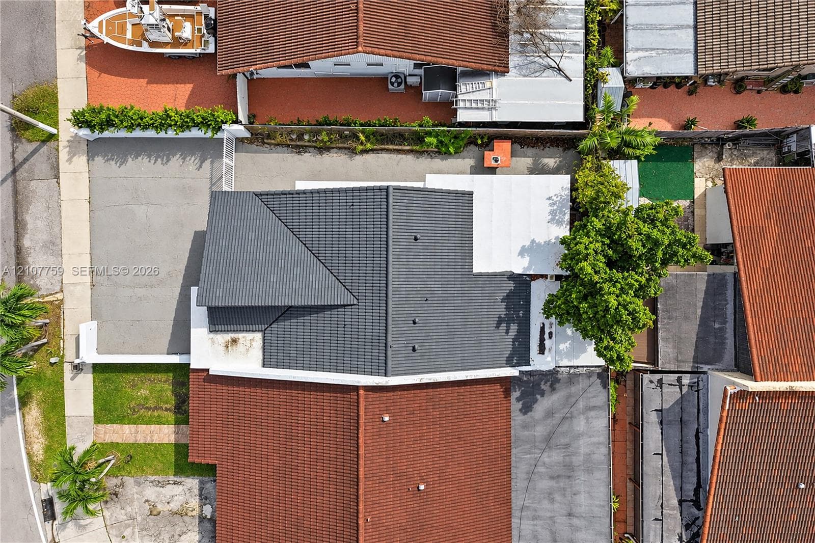 Aerial view featuring a dark-toned tile roof, an asphalt-paved driveway, and a white covered patio structure