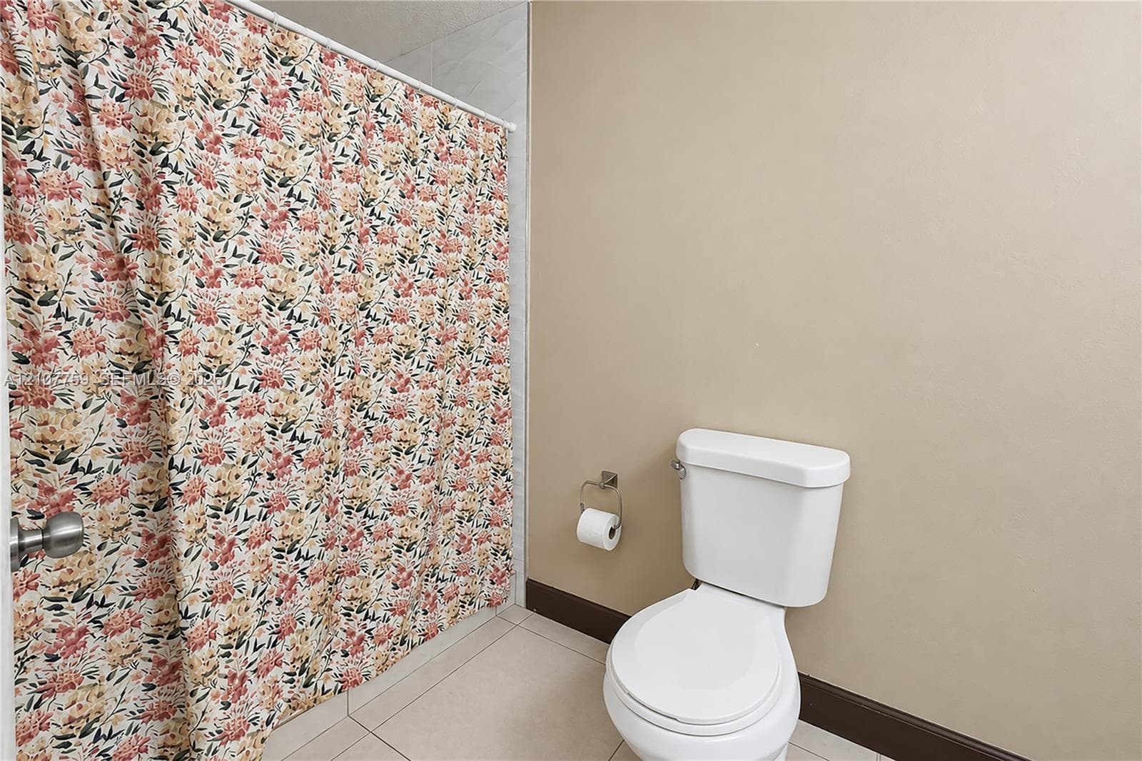Bathroom featuring a white ceramic toilet, tiled flooring, and a wall-mounted metal toilet paper holder