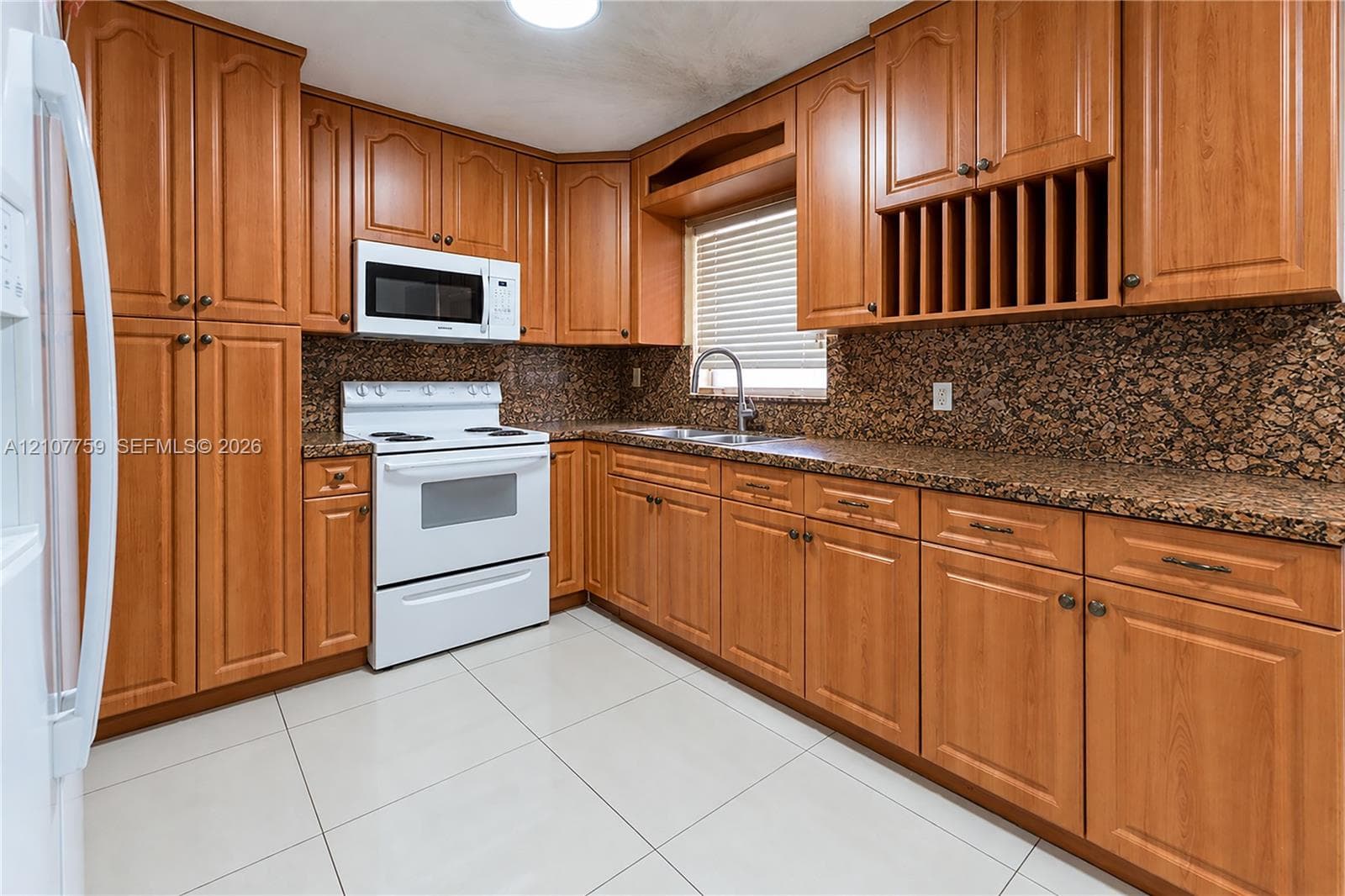Kitchen featuring wood cabinetry, integrated wine storage, stone-finish countertops, tile flooring, and white appliances
