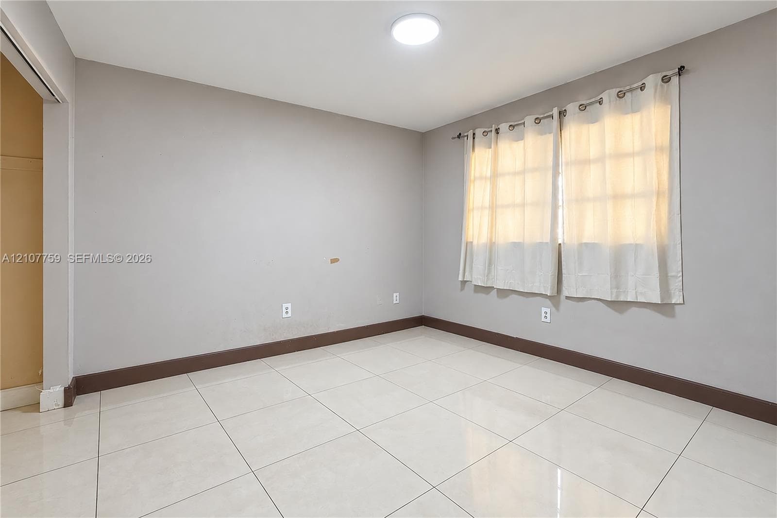 Neutral-toned walls, large-format tile flooring, and a multi-pane window with a curtain rod fixture