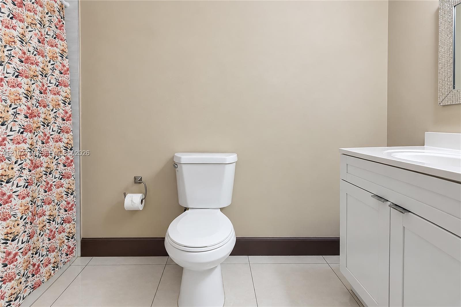 Bathroom featuring a white vanity cabinet with an integrated sink and countertop, light-toned tile flooring, and a wall-mounted toilet