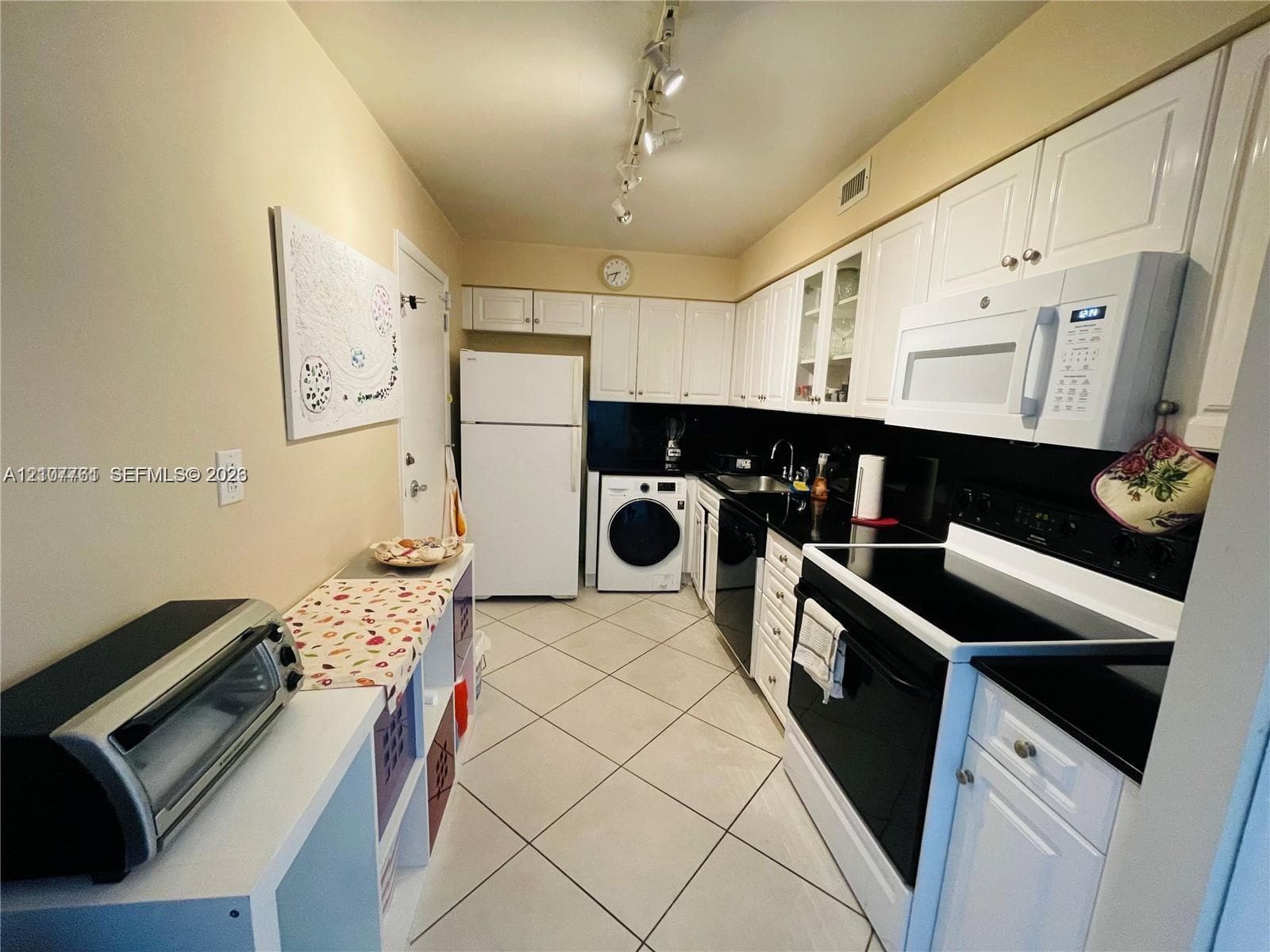 Kitchen featuring white cabinetry, black countertops, integrated laundry appliances, tile flooring, and track lighting