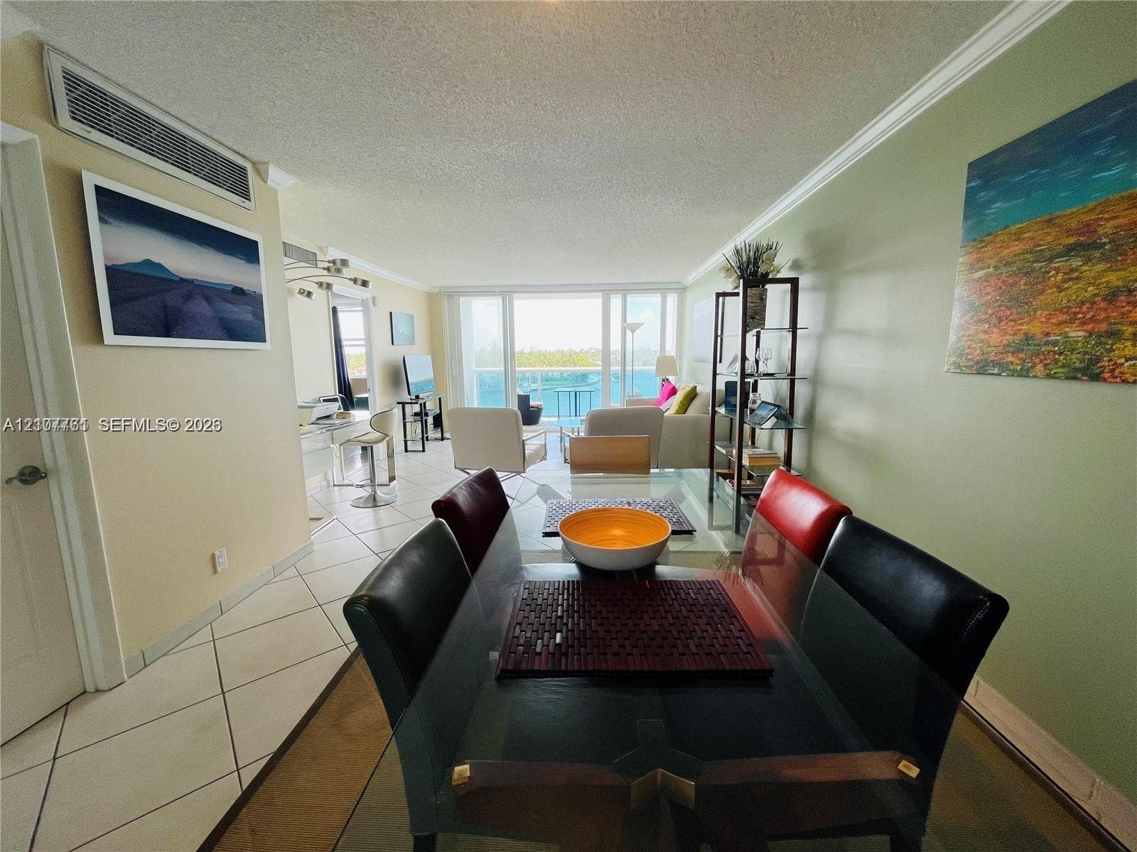 Open-concept interior featuring large-format tile flooring, crown molding, wall-mounted climate control system, and sliding glass doors with access to an exterior balcony