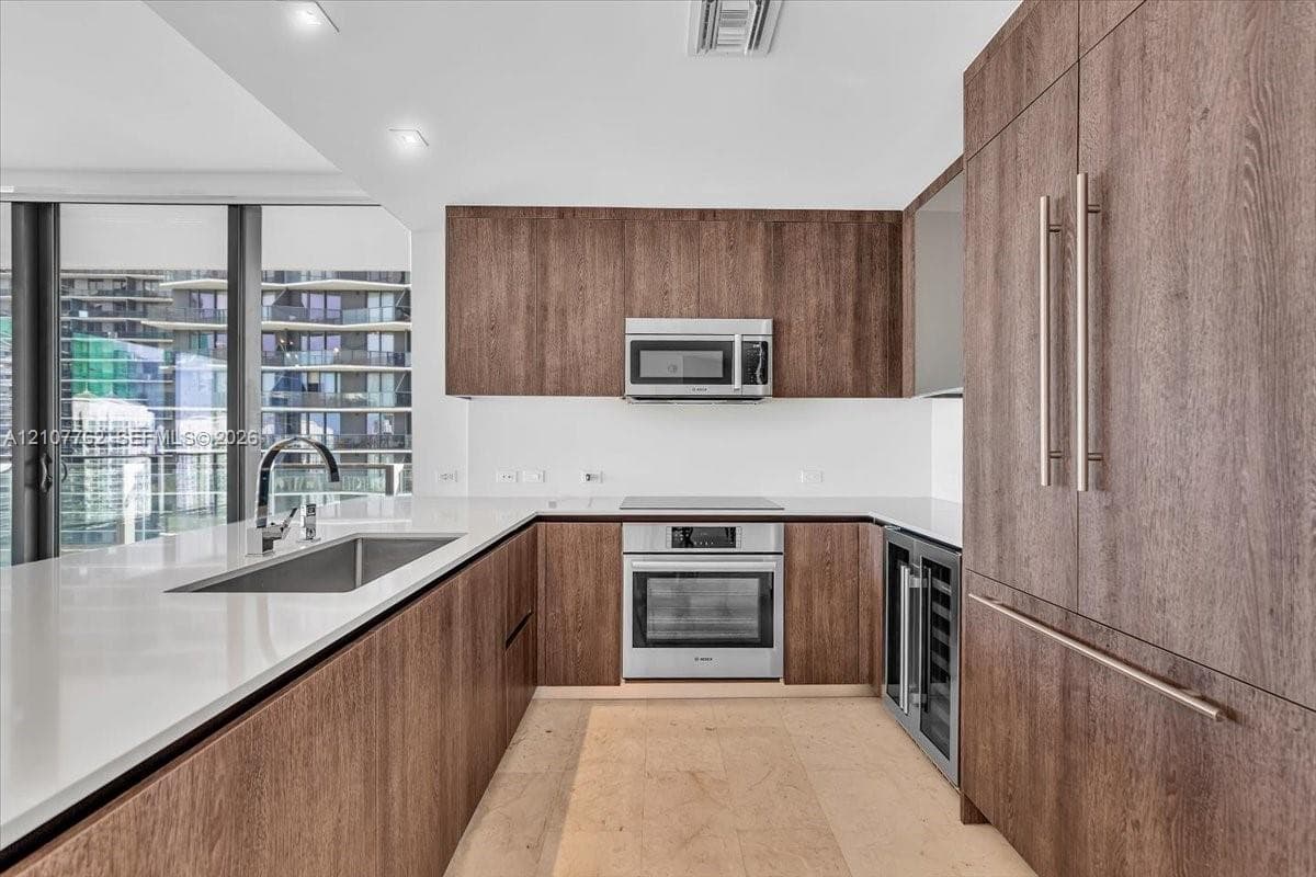 Contemporary kitchen featuring wood-finish cabinetry, quartz countertops, stainless steel appliances, an integrated wine refrigerator, and floor-to-ceiling windows