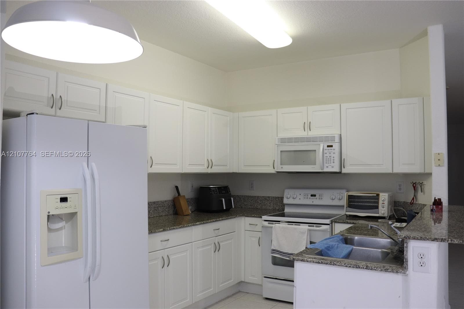 Kitchen featuring white cabinetry, stone-surface countertops, dual-basin stainless steel sink, and white appliances including a built-in microwave and refrigerator