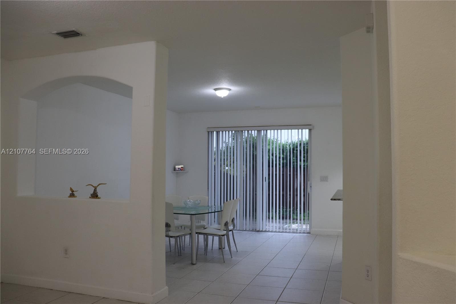 Interior featuring arched wall niche, neutral tile flooring, and sliding glass doors with vertical blinds