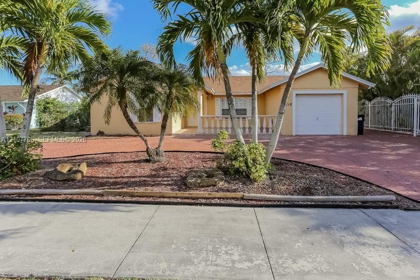 Single-story residence featuring a stucco exterior, paved driveway, single-car garage, balustrade-style porch railing, and established palm landscaping