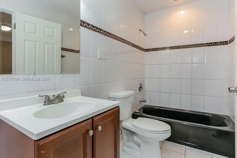 Bathroom featuring a wood-finish vanity with a white integrated sink, a deep-set black soaking tub, white wall tiling with decorative accent inlay, and a wall-mounted rectangular mirror